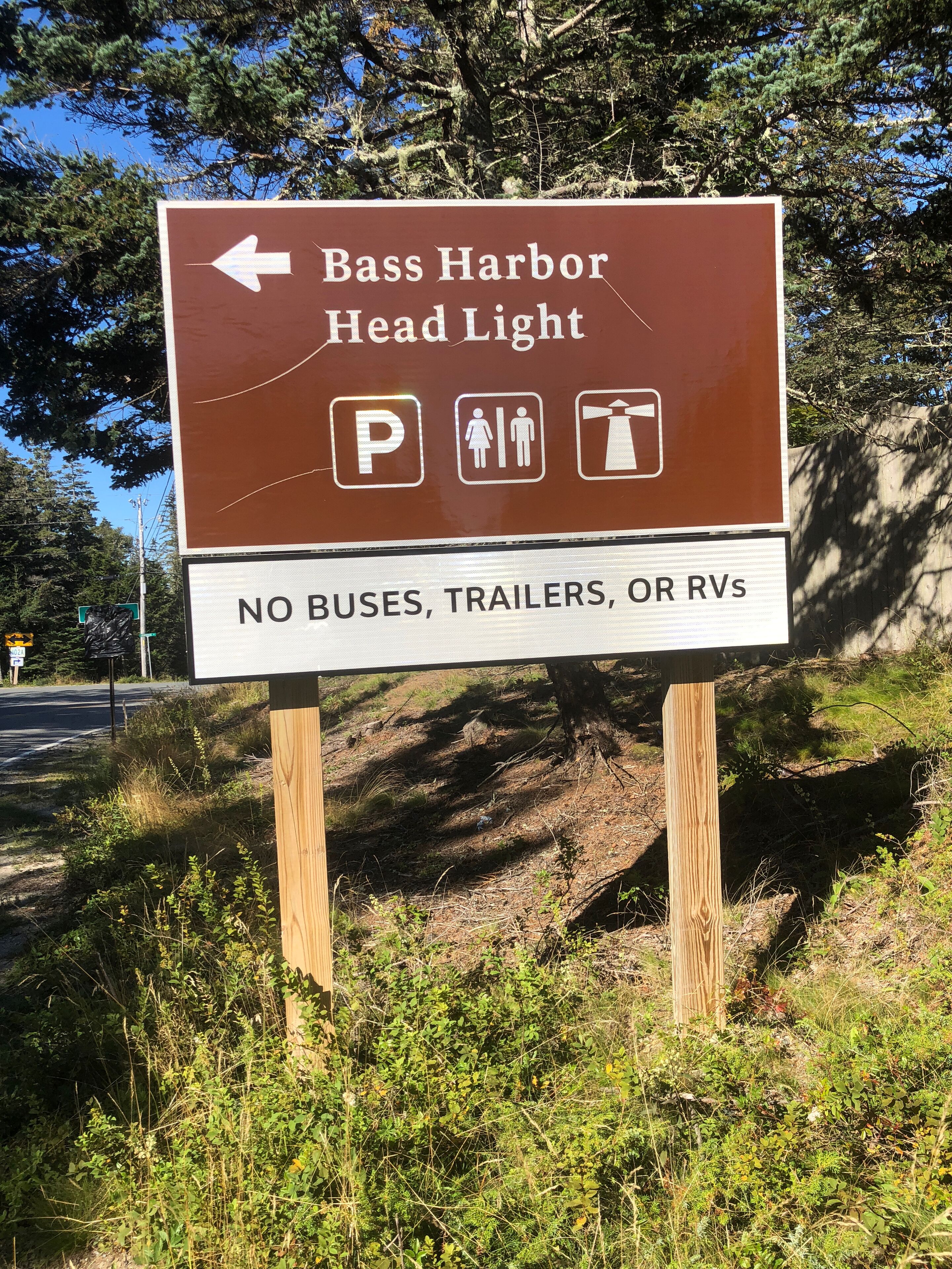 Un panneau de signalisation indiquant la direction du phare de Bass Harbor, avec des symboles représentant les aires de stationnement et les toilettes, ainsi qu’une indication interdisant l’accès aux autobus, aux remorques et aux véhicules récréatifs.
