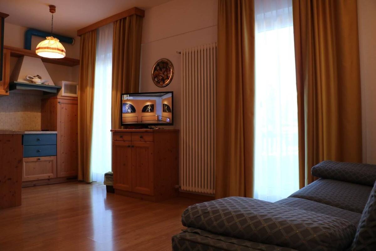 A cozy room with a wooden floor, a sofa, a TV on a wooden cabinet, and a window with curtains.