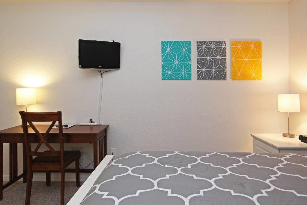 A hotel room with a bed, a desk, a chair, a TV, and three wall-mounted artworks.