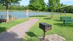 Un área de picnic con un sendero pavimentado, mesas de picnic, un buzón y una señal de parada junto a un lago.