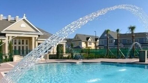 Una piscina con fuente, rodeada de una valla y edificios residenciales al fondo.