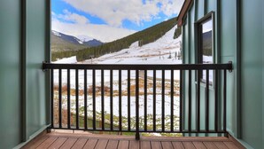A balcony with a metal railing overlooking a snowy landscape with trees and mountains.