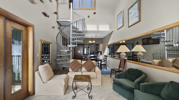 A spacious living room with a spiral staircase, a dining area, and a kitchen in the background.