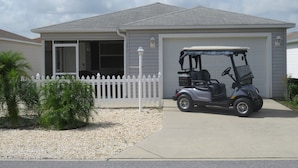 A single-story house with a garage, a white picket fence, and a golf cart parked in front. - Patio Villa in Duval Village - Gas Golf Cart INCLUDED - 5 minutes to everywhere (The Villages)