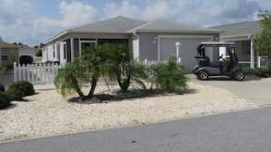 A residential house with a garage, a white picket fence, and a golf cart parked in the driveway. - Patio Villa in Duval Village - Gas Golf Cart INCLUDED - 5 minutes to everywhere (The Villages)