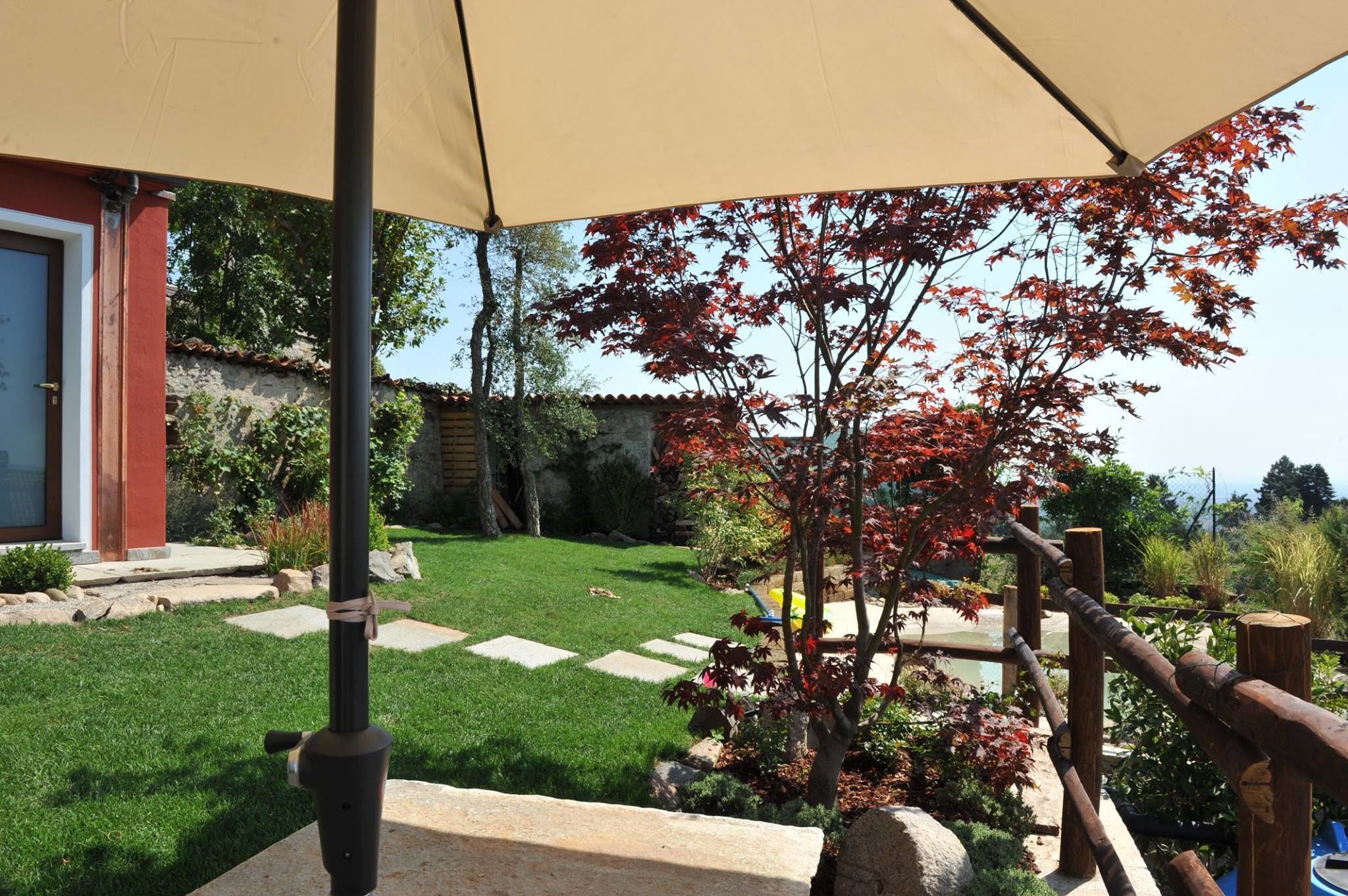 Un jardín cuidado con un sendero de piedra, una valla de madera y una sombrilla beige que da sombra.