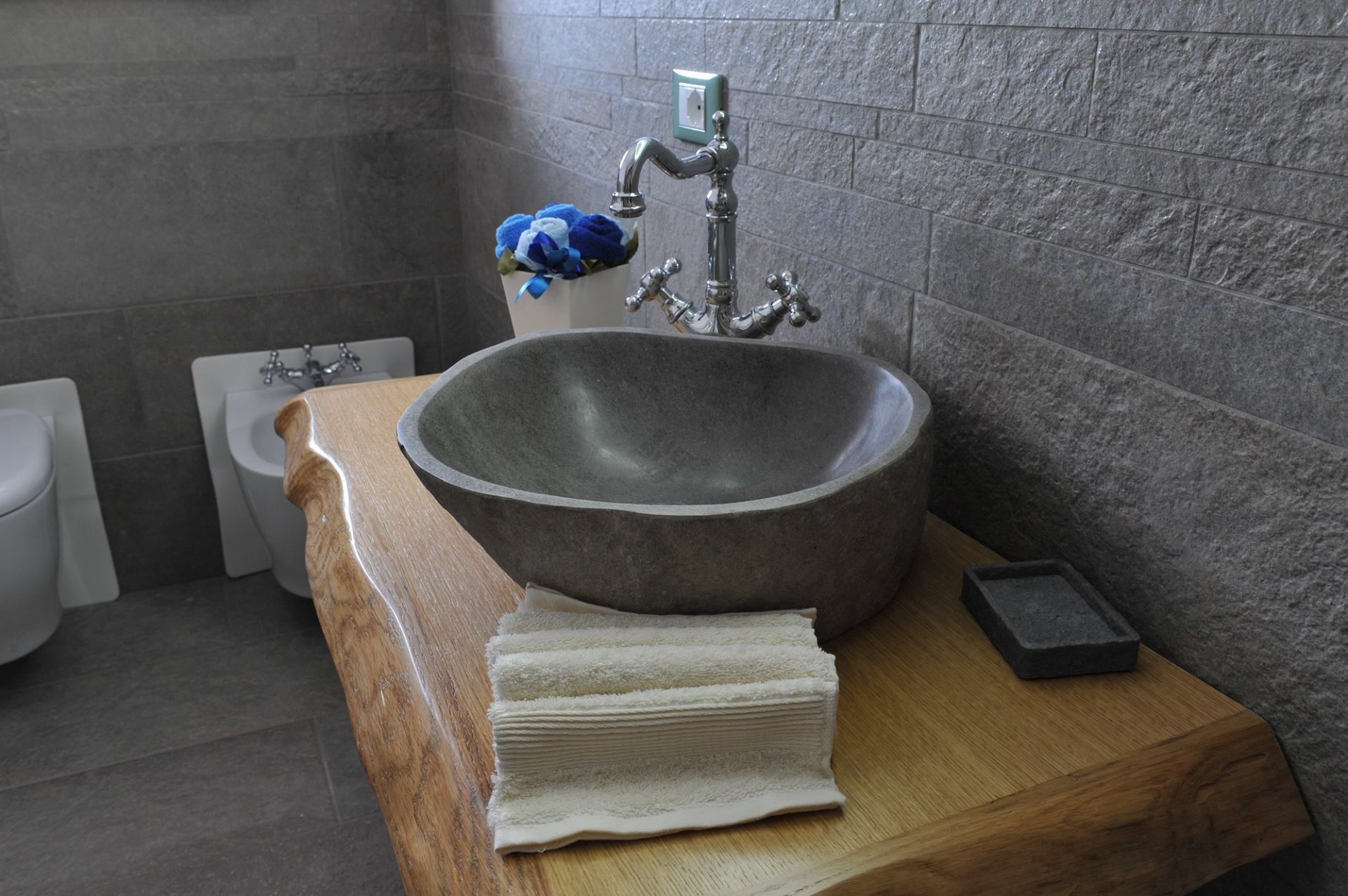 A bathroom with a large stone sink, a wooden counter, a toilet, and a blue towel on the wall.