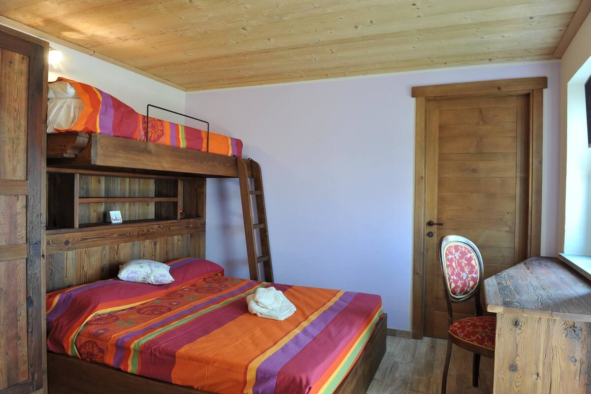 A bunk bed with a colorful blanket, a wooden desk, and a chair with a floral cushion.