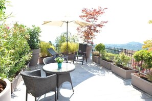 An outdoor patio with wicker furniture, a table with a vase, potted plants, and a view of the mountains. - Affittacamere Belvedere (Sordevolo)