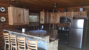 Cocina con armarios de madera, encimera de granito, refrigerador de acero inoxidable e isla de piedra con taburetes de bar.