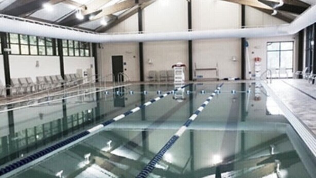 Una piscina interior con carriles delimitados, un trampolín y un techo alto con vigas a la vista.