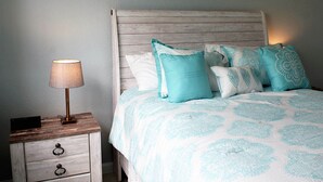 A bed with a wooden headboard and a white and blue patterned bedspread. There is a nightstand with a lamp and a drawer. - Magical Florida Getaway. (Davenport)