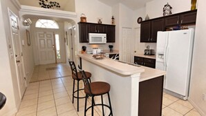 A kitchen with a central island, two bar stools, dark cabinets, a white refrigerator, and a microwave. - Glenbrook Retreat (Clermont)