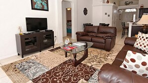 A living room with a brown leather sofa, a glass coffee table, and a television on a dark wooden stand. - Glenbrook Retreat (Clermont)
