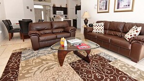 A living room with a brown leather sofa, a glass coffee table, and a patterned rug. There is a dining area with chairs and a table in the background. - Glenbrook Retreat (Clermont)