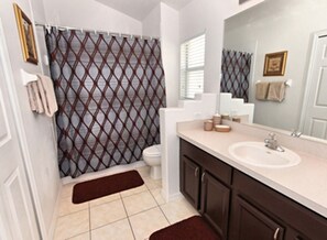 A bathroom with a shower curtain, toilet, sink, and cabinets.