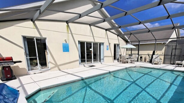A swimming pool with a clear blue water, surrounded by a covered area with chairs and tables. - Glenbrook Retreat (Clermont)