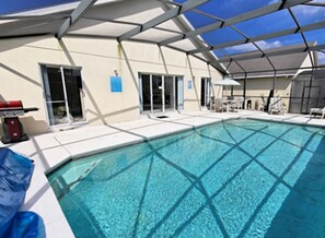 A swimming pool with a clear blue water, surrounded by a covered area with chairs and tables.
