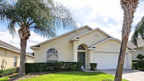 A single-story house with a front garage, a small front yard with grass and a few shrubs, and two palm trees. - Glenbrook Retreat (Clermont)