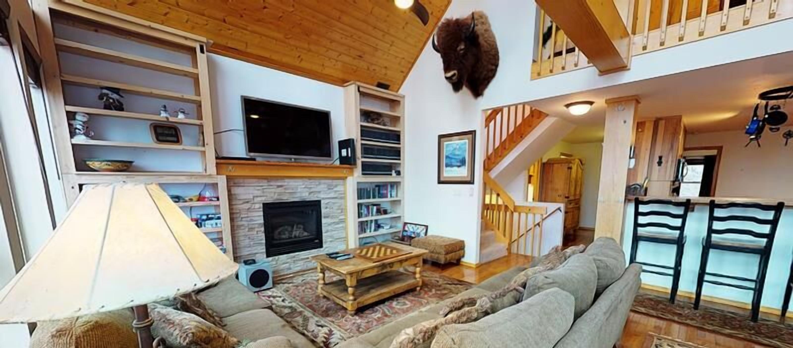 A spacious living room with a fireplace, a television, and a staircase leading to an upper level.