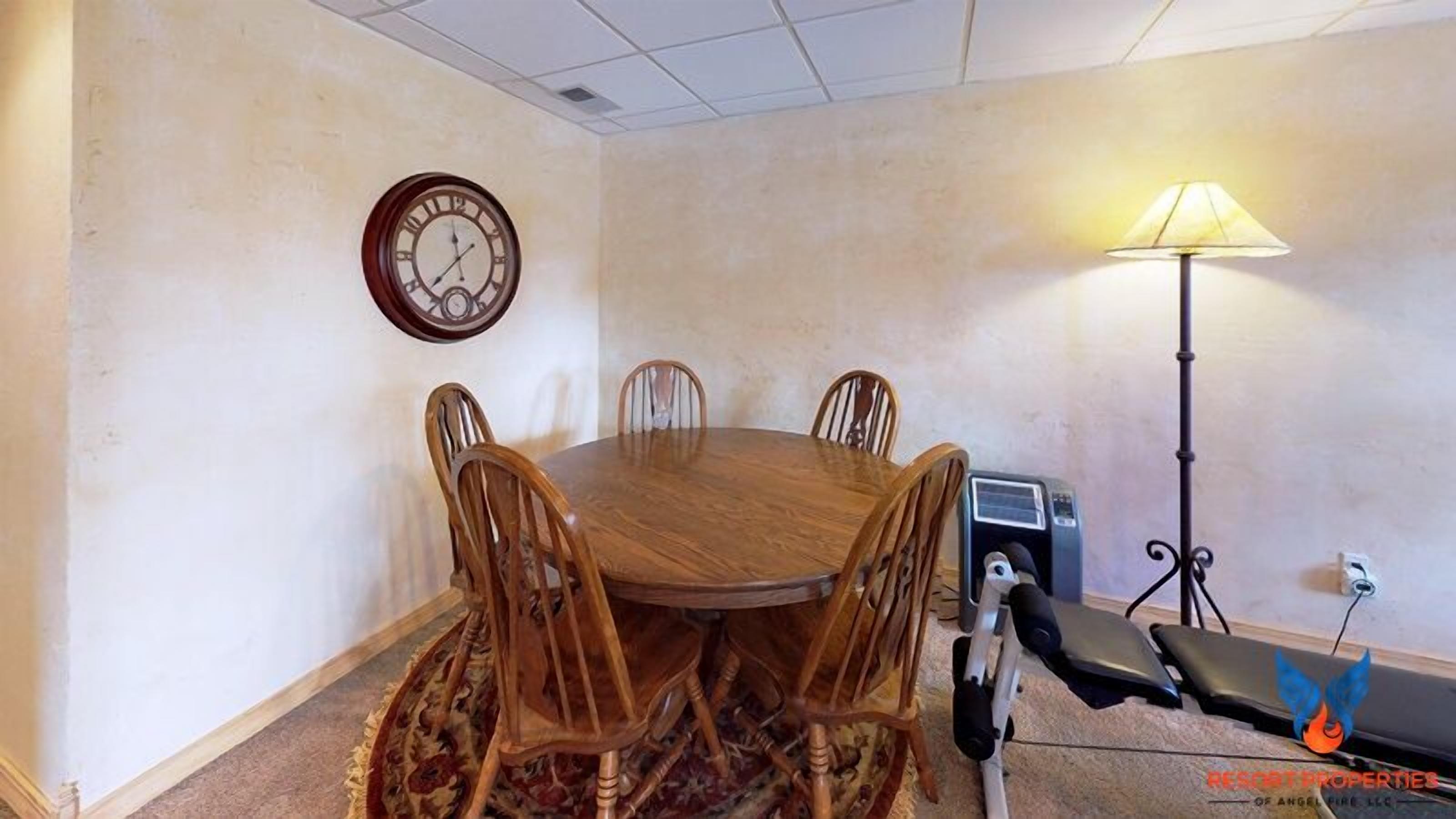 A conference room with a wooden table, six chairs, a clock, a lamp, and a wheelchair.