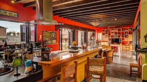 A spacious bar area with a wooden counter and bar stools, a large open kitchen with red walls, and a bookshelf filled with books and decorative items. - Private, Staffed Old Vallarta Casa with Rooftop Views, Art, Pool, & Walkability (Puerto Vallarta)