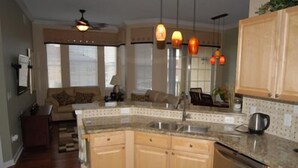 A kitchen with wooden cabinets, a granite countertop, a built-in dishwasher, and pendant lighting. - Kumar's Kastle (Davenport)