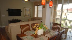 A dining area with a wooden table set for four, a sofa in the background, and a balcony with a view. - Kumar's Kastle (Davenport)