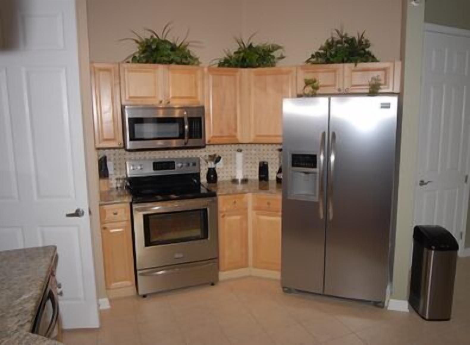 A compact kitchen with wooden cabinets, a stainless steel refrigerator, a microwave, an oven, and a sink.