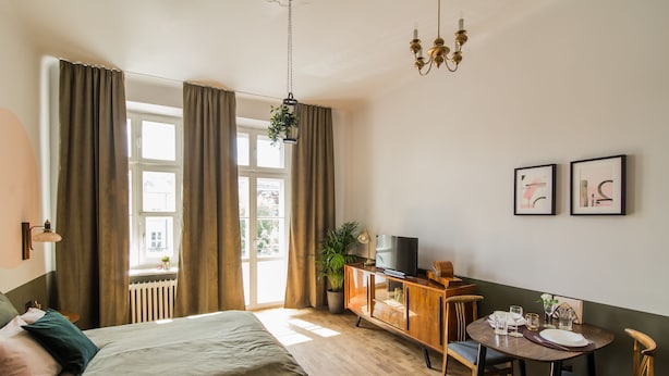 A hotel room with a bed, a dining table with chairs, a TV on a wooden cabinet, and two framed pictures on the wall. - Aparthotel Nowy Świat 28 (Warsaw)
