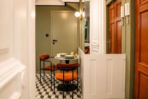 A narrow hallway with a checkered floor leading to a dining area with two chairs and a table set with plates, cups, and a candle. - Aparthotel Nowy Świat 28 (Warsaw)
