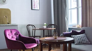 A cozy living room with a purple armchair, a wooden coffee table, and a sofa with patterned cushions. - Aparthotel Nowy Świat 28 (Warsaw)