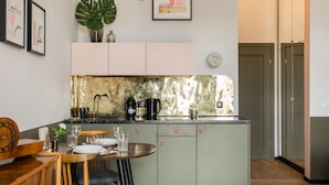 A compact kitchen with a central island, a dining area with a wooden table and chairs, and a large plant on the wall. - Aparthotel Nowy Świat 28 (Warsaw)