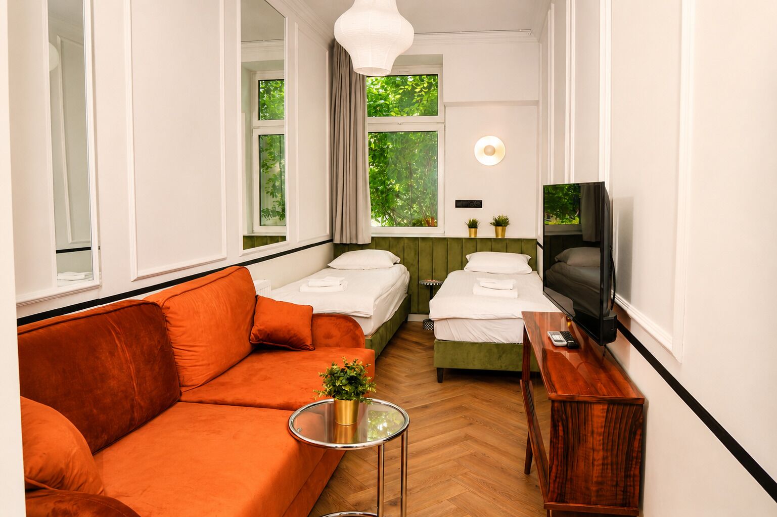 A hotel room with a sofa, two beds, a TV, and a small table with a plant.
