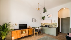 A modern living room with a wooden TV stand, a dining table, and a kitchen area with a countertop and cabinets. - Aparthotel Nowy Świat 28 (Warsaw)