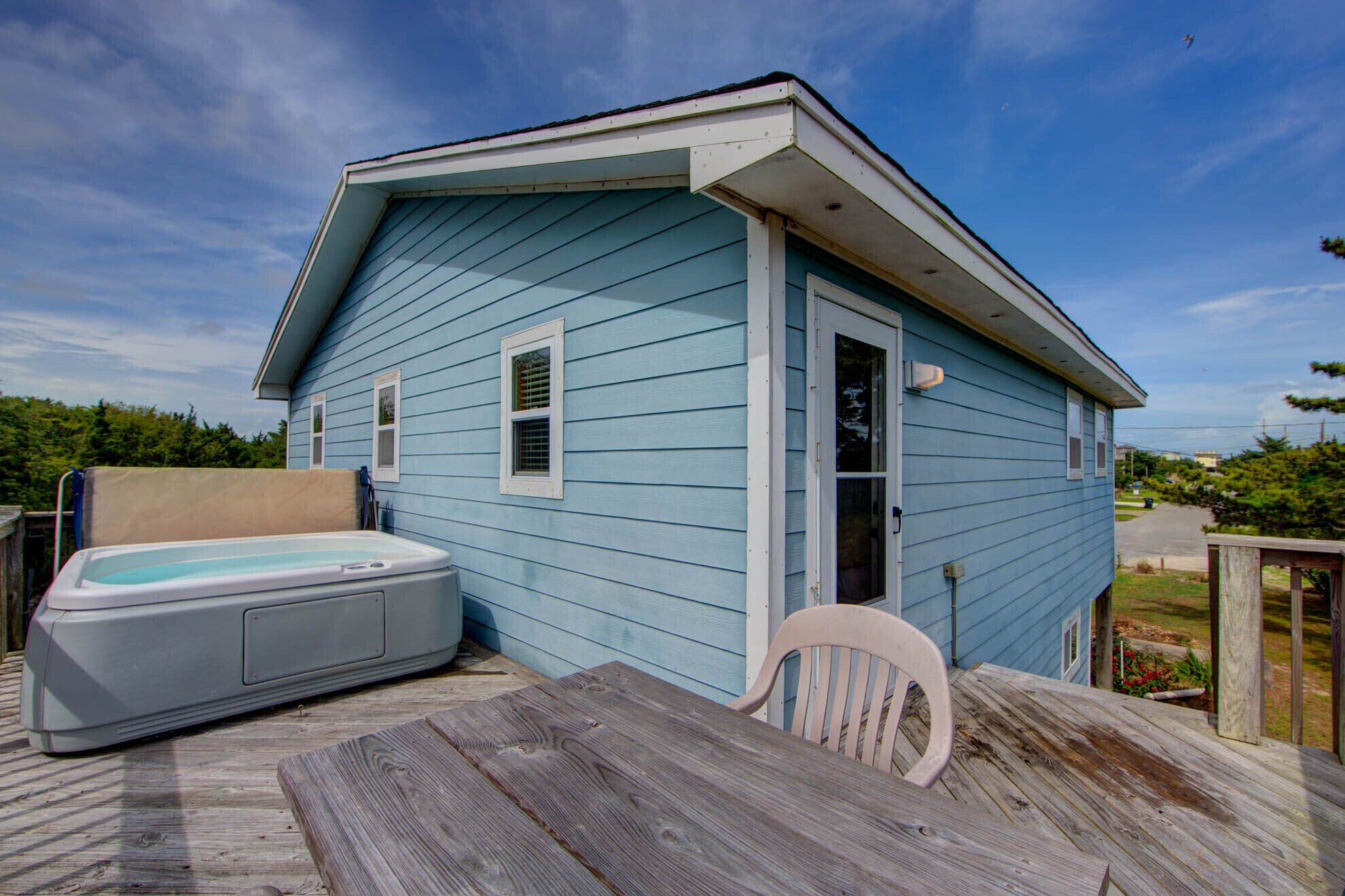 A small blue house with a hot tub and a wooden deck.