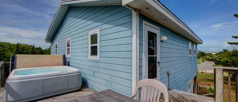A small blue house with a hot tub and a wooden deck.