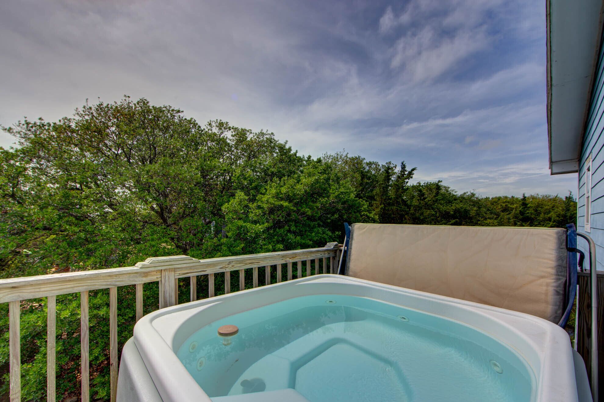 A hot tub on a wooden deck with a view of trees and a cloudy sky.