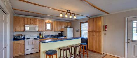A kitchen with wooden cabinets, a central island with stools, a microwave, a stove, and a refrigerator.