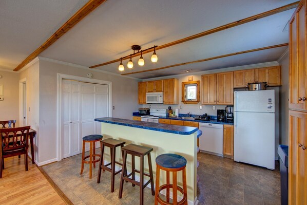 A kitchen with wooden cabinets, a central island with stools, a microwave, a refrigerator, and a ceiling light fixture. - Casa Creekside w/ hot tub and bikes! (Avon)