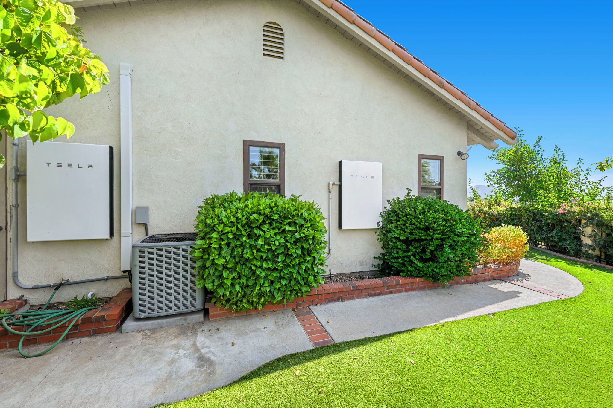 A building with two Tesla charging stations, a brick pathway, and well-maintained green lawns.