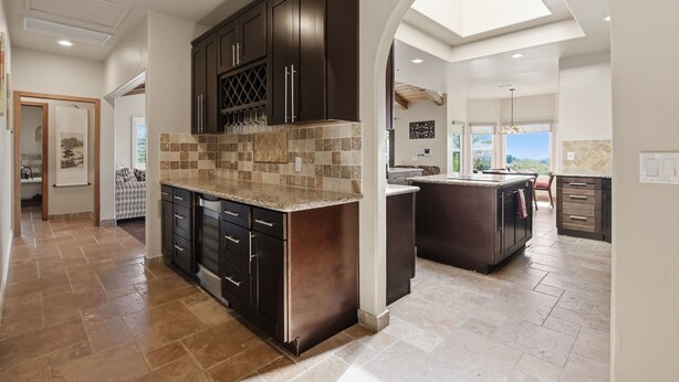 A modern kitchen with dark cabinetry, a tiled backsplash, and a skylight.