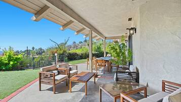Un espace extérieur aménagé en terrasse, avec des meubles en bois, une table en verre et une vue sur un jardin paysager.