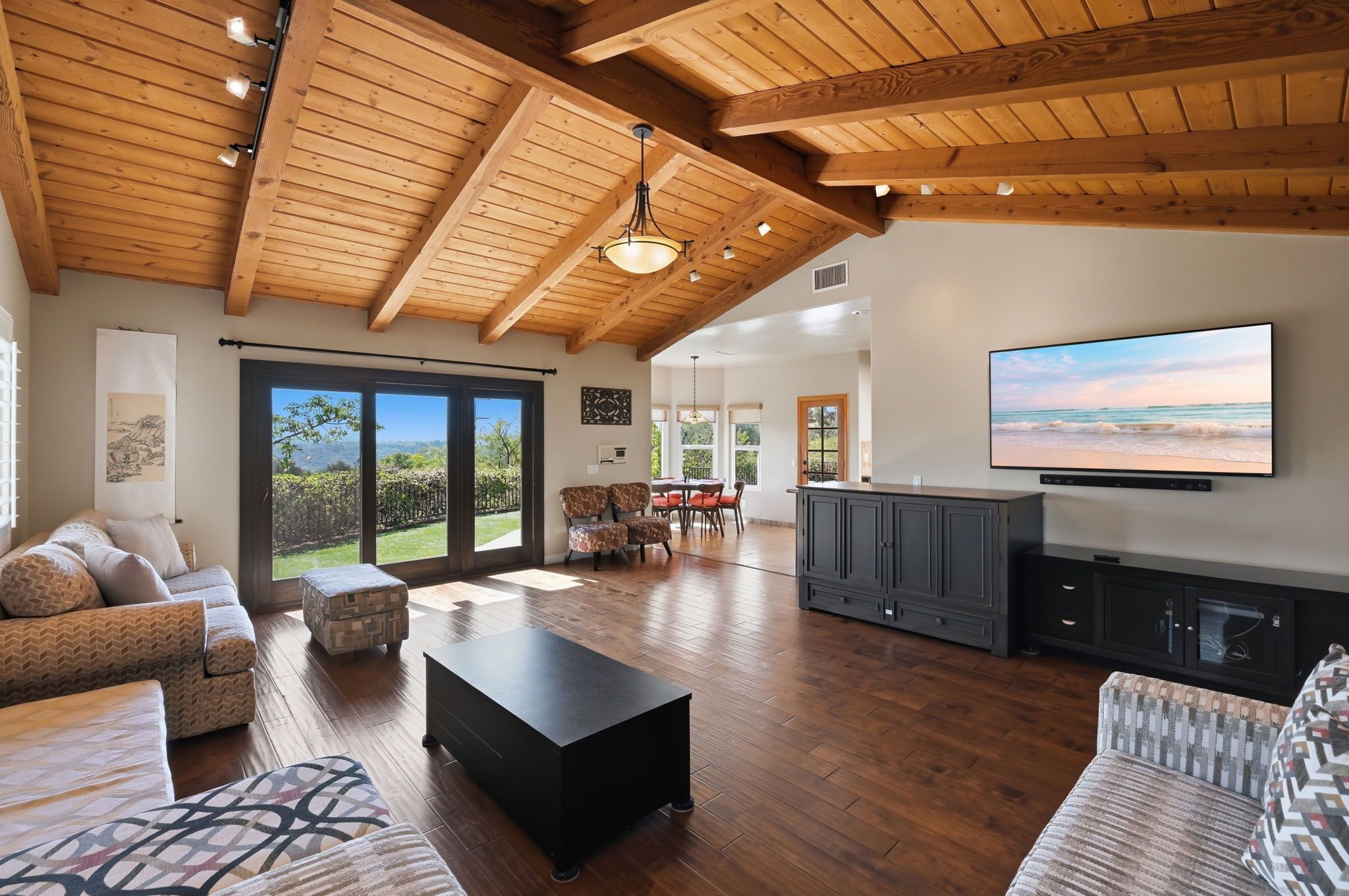 Amplia sala de estar con techo de madera, televisor grande y vistas al exterior.