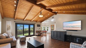 A spacious living room with a wooden ceiling, a large TV, and a view of the outdoors.