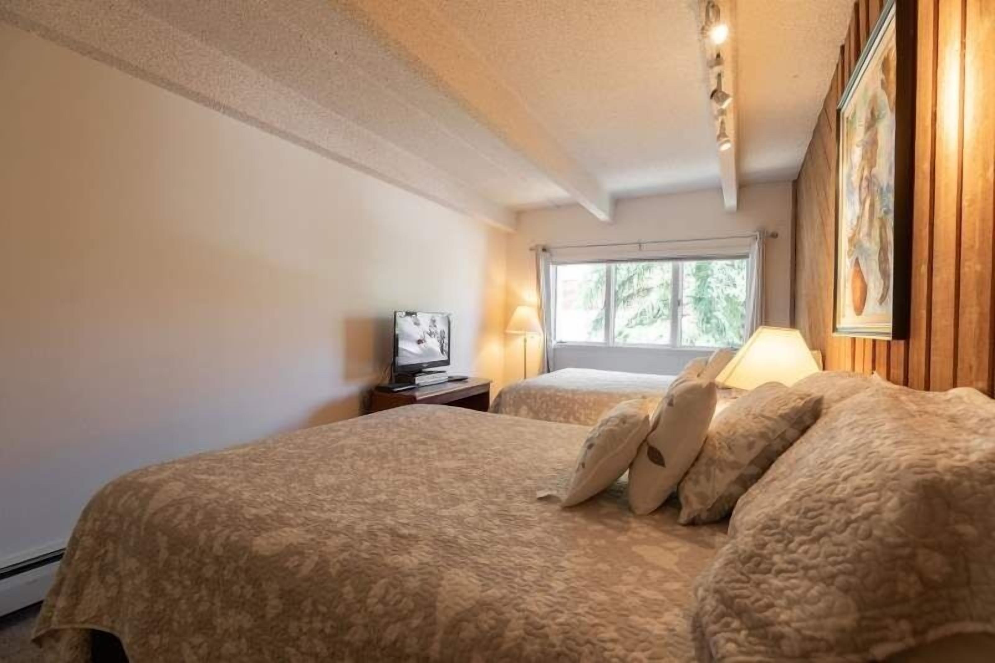 Een hotelkamer met twee bedden, een televisie op een nachtkastje en een raam met uitzicht op bomen.