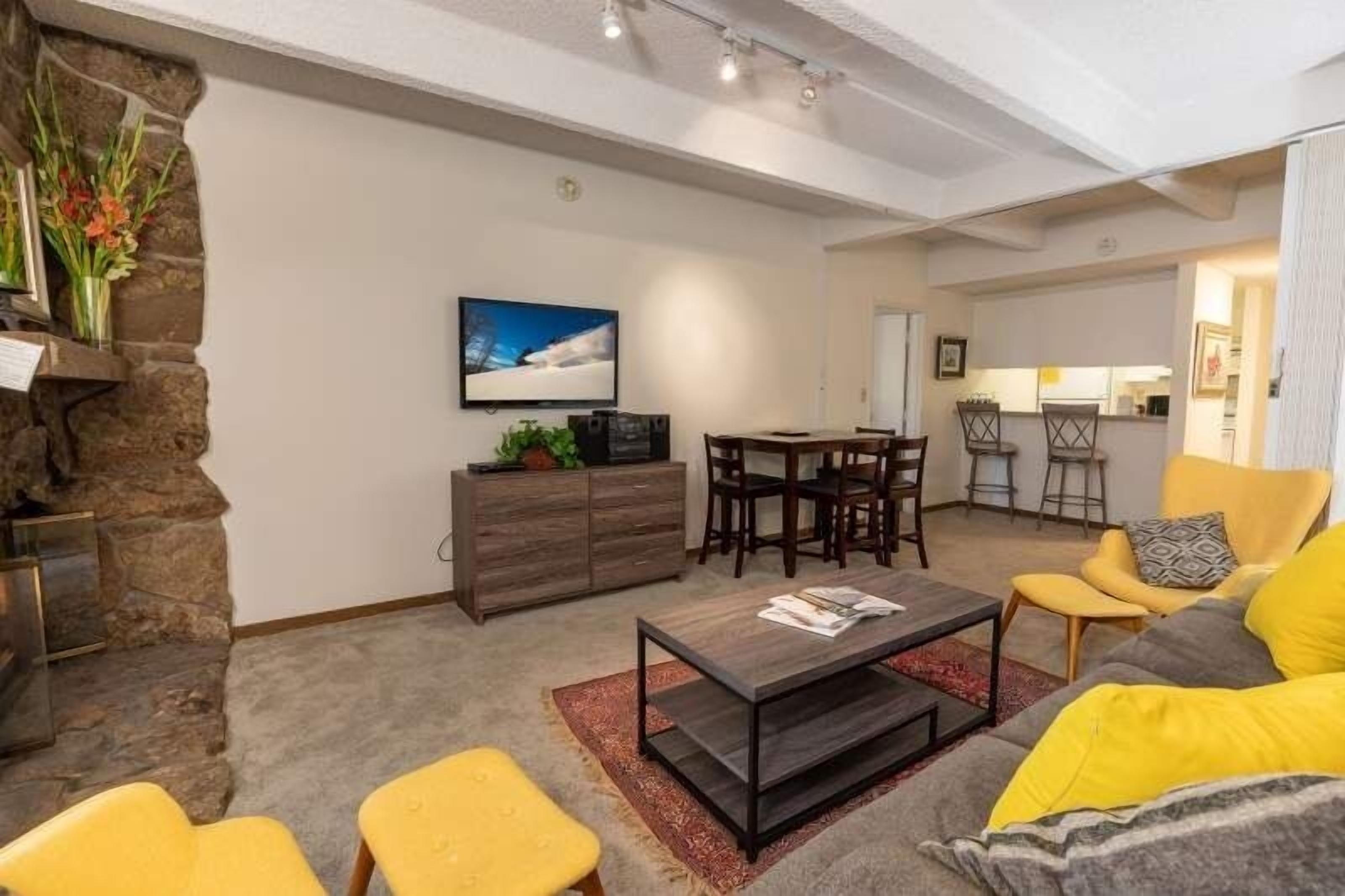 Ein modernes Wohnzimmer mit einer Wand aus Stein, einem Fernseher, einem Essbereich und einer Küche im Hintergrund.