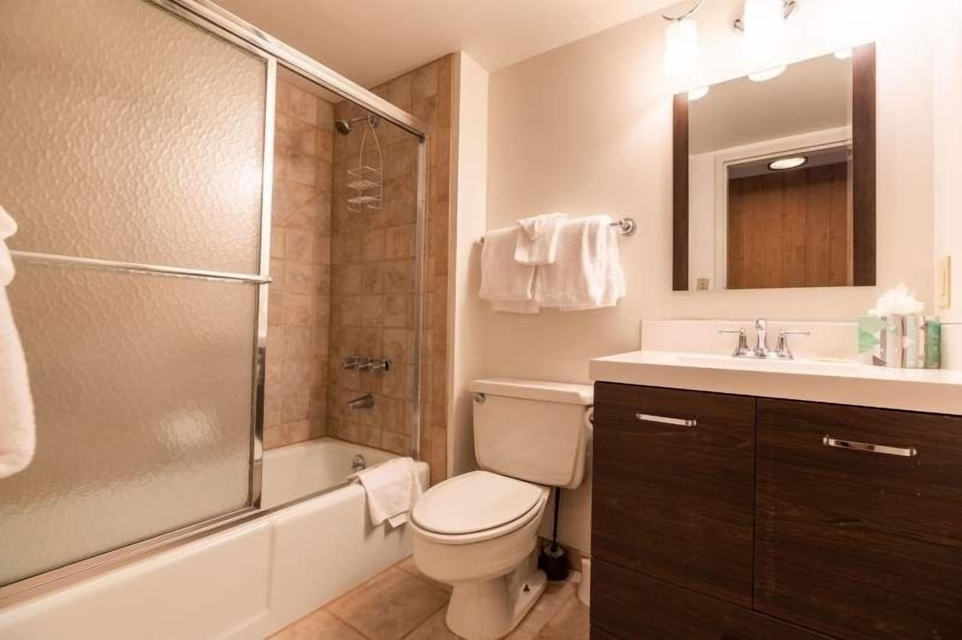 A bathroom with a glass shower enclosure, a toilet, a bathtub, and dark wooden cabinets.