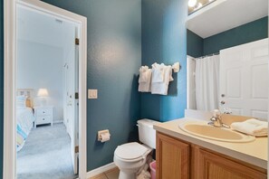 A bathroom with a blue wall, white toilet, and a sink with a mirror above it. - Regal Retreat (Davenport)