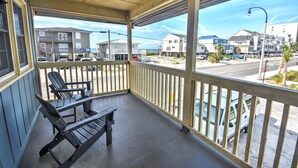 A covered balcony with two Adirondack chairs and a table, overlooking a street with cars and buildings. - 202 28th Ave Unit 6 1 Bedroom Condo (North Myrtle Beach)